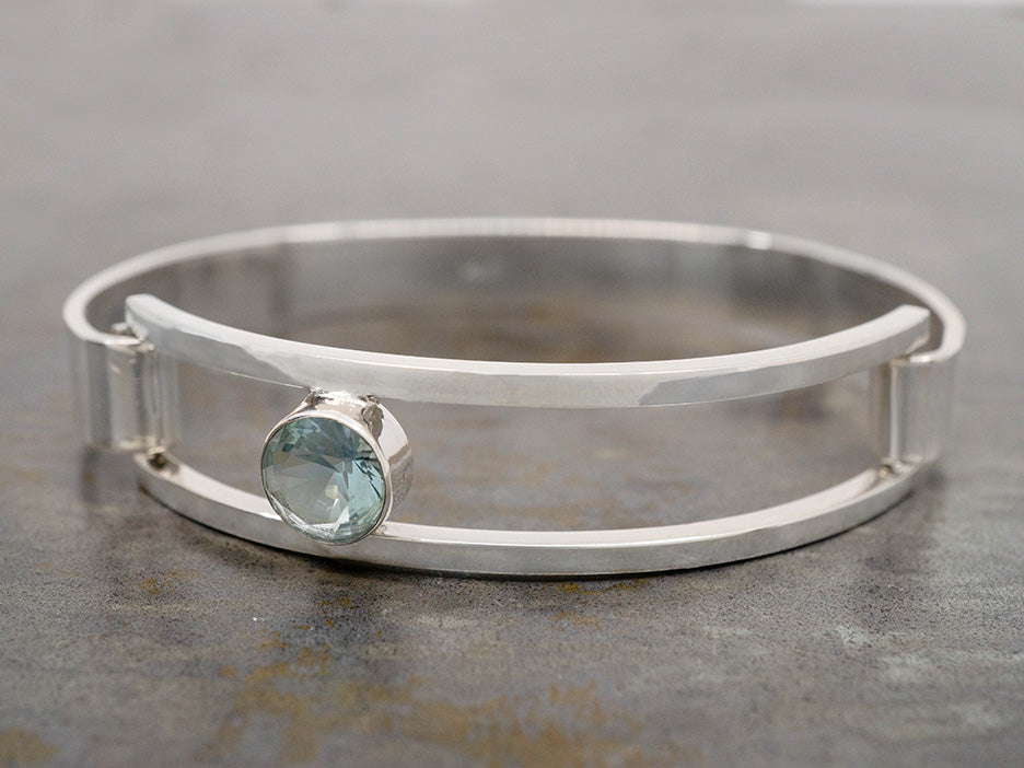 A sterling silver hinged bracelet with an off-center light blue crystal