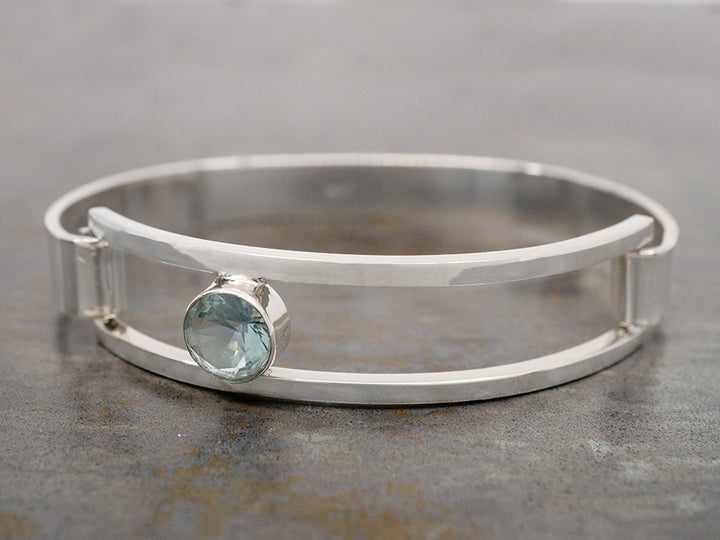 A sterling silver hinged bracelet with an off-center light blue crystal