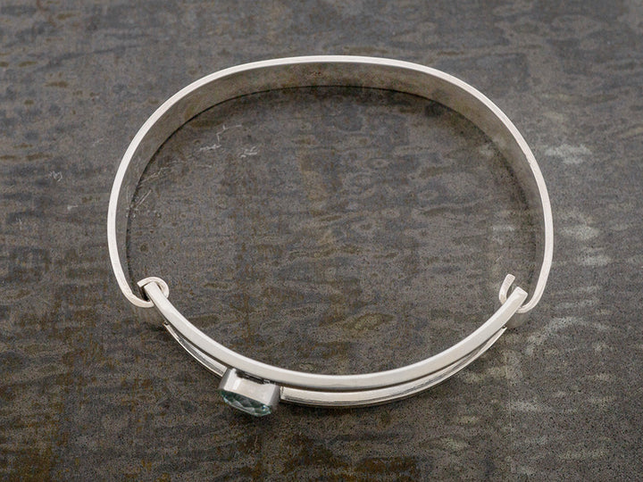 A sterling silver hinged bangle with an off-center blue crystal