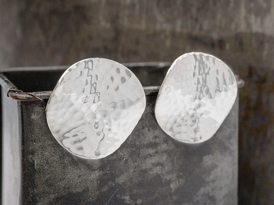 A pair of post earrings that are two hammered, silver disc.