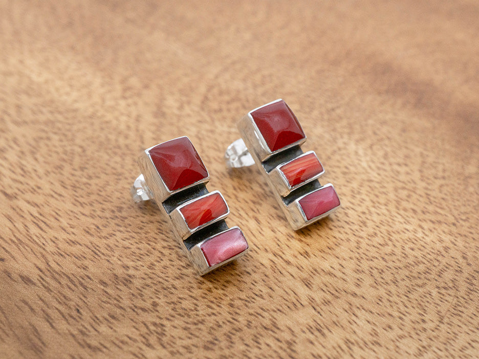 A pair of sterling silver post earrings that have three vertically set stones of red and pink hues.