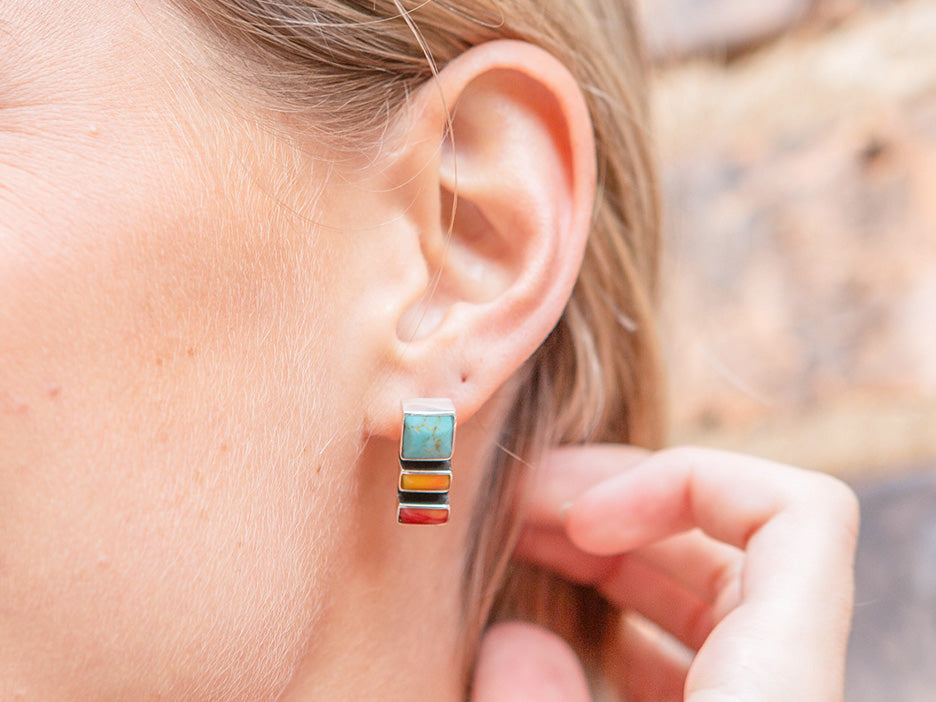 A model wearing a sterling silver earring featuring three stones, one turquoise, one yellow and one coral.