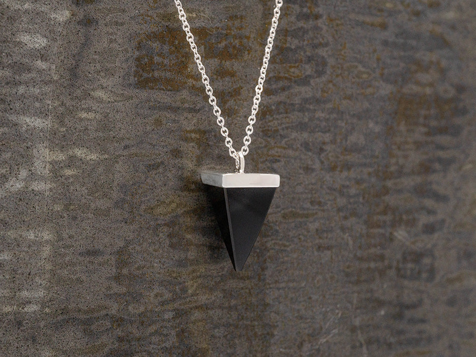 An obsidian pyramid pendant hanging on a sterling silver chain with the point facing down.