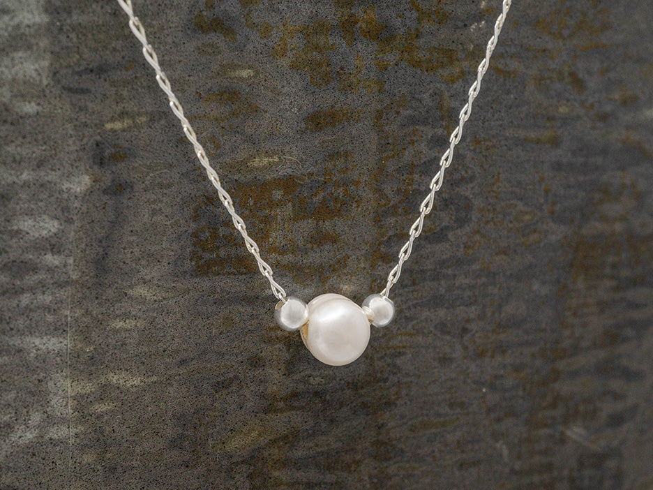 A single white pearl on a silver chain with small silver beads on either side.