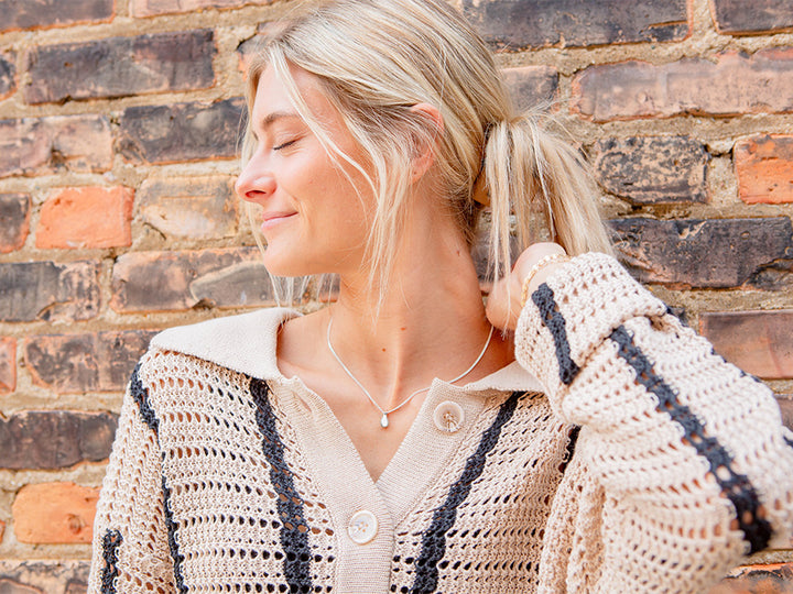A model wearing a dainty sterling silver necklace with a teardrop in the center.