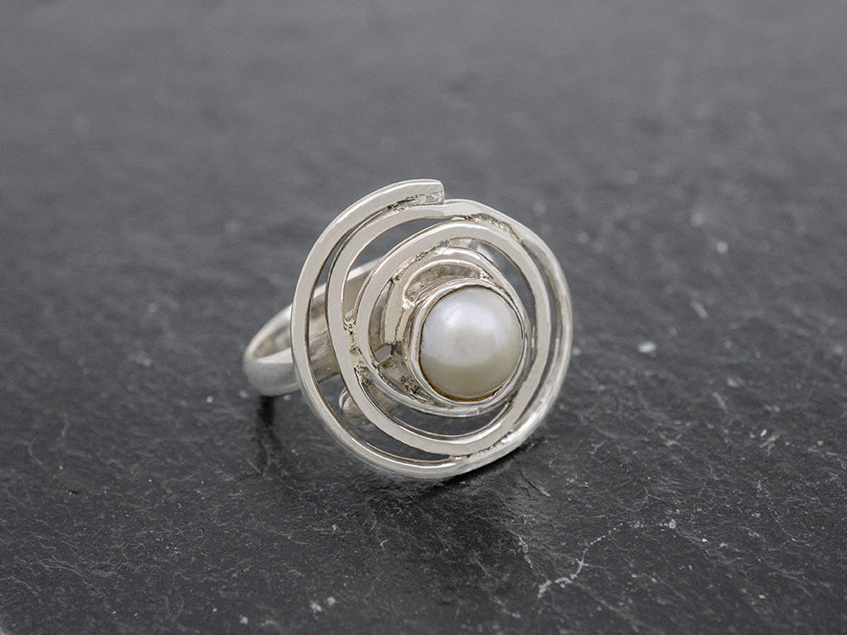 An adjustable ring featuring a cultured pearl at the center of a silver swirl.