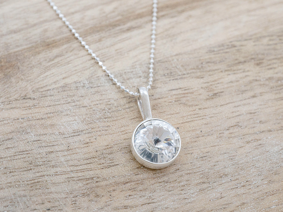 A round, clear crystal pendant set in sterling silver on a sterling silver chain.