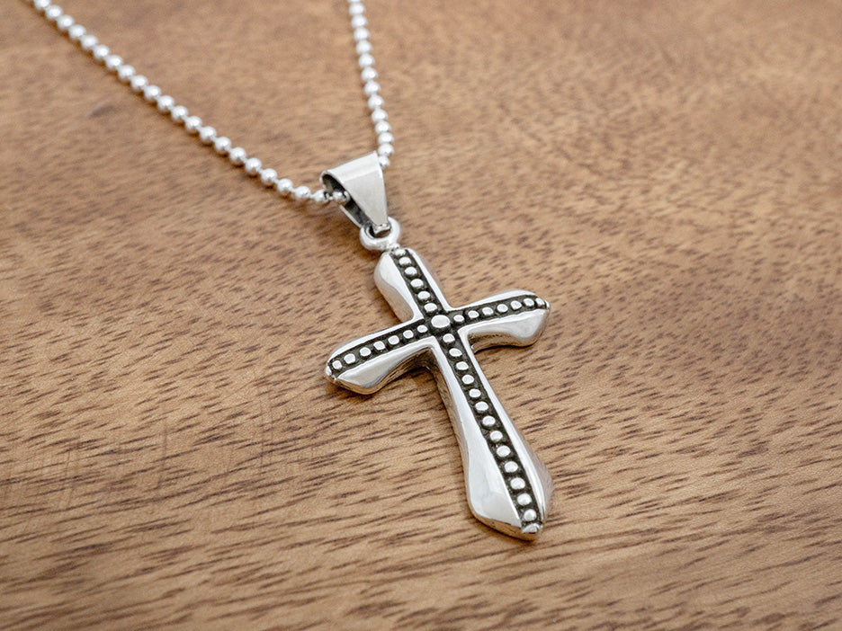 A sterling silver cross pendant with oxidized channels cut into it with beads sitting in the channels.