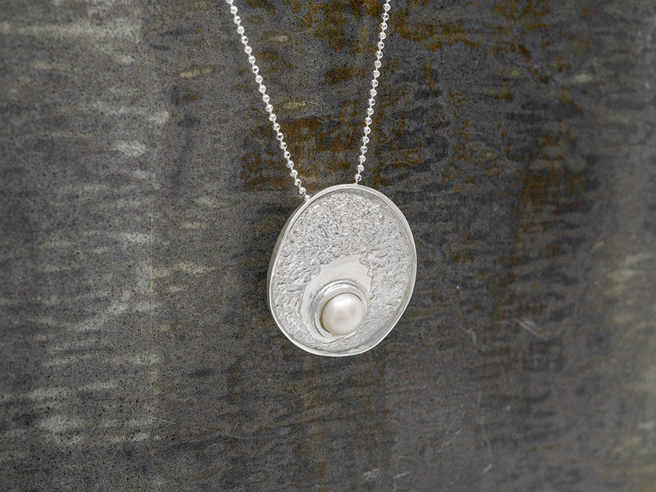 A texture sterling silver disc pendant with an off-center pearl