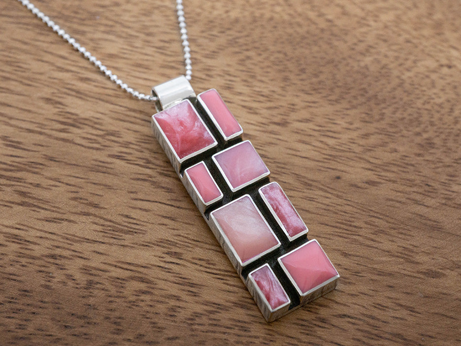 A rectangular pendant made of a mosaic of shades of pink.