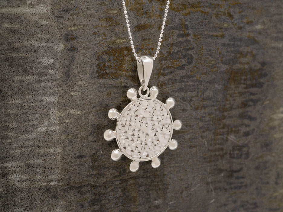 A hammered silver disc pendant with beads spaced around outside its frame.
