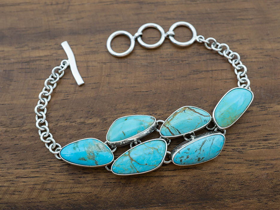 A sterling silver bracelet featuring a cluster of genuine turquoise stones in the center.