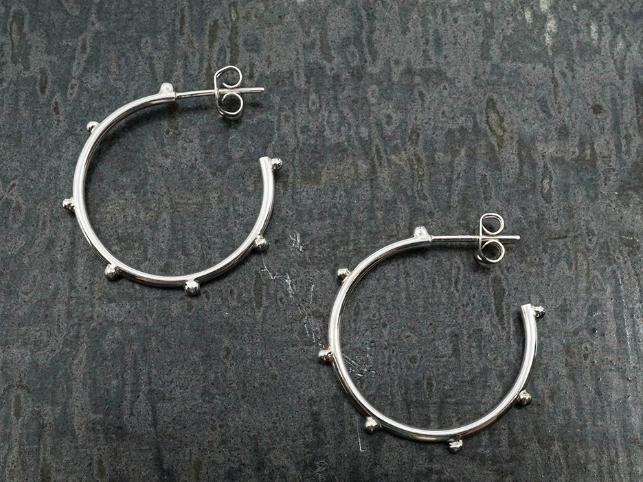 a pair of sterling silver hoop earrings with beads spaced around the outside.