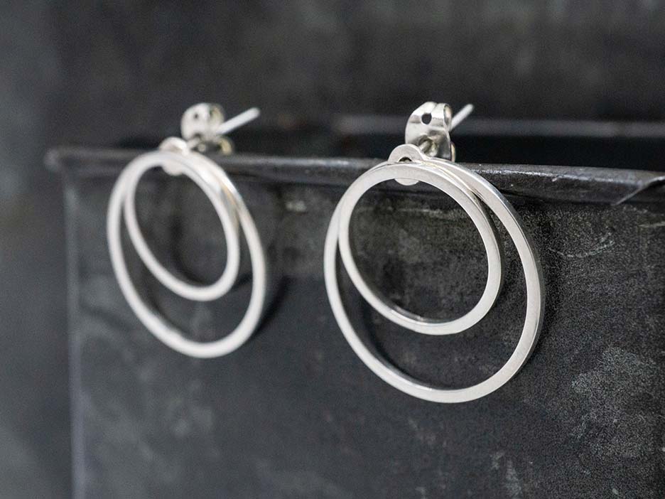 A sterling silver earring comprised of two concentric circles. The larger of the two circles is a jacket that can be removed, worn behind the earlobe or stacked behind the smaller circle.