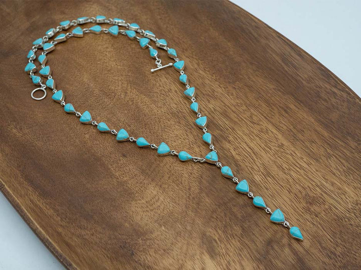 A sterling silver lariat necklace made with turquoise stones cut into teardrop and trillion shapes.