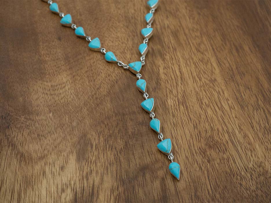 A sterling silver lariat necklace made with turquoise stones cut into teardrop and trillion shapes.