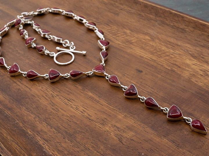 A sterling silver lariat necklace made with teardrop and trillion cut red jasper stones. The necklace has a toggle closure..