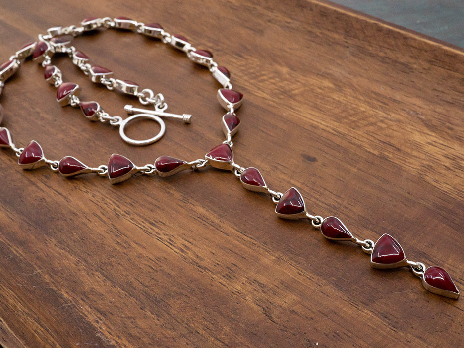 A sterling silver lariat necklace made with teardrop and trillion cut red jasper stones. The necklace has a toggle closure..