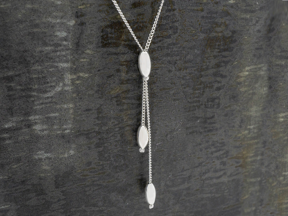 Sterling silver lariat necklace with an elliptical bead at the center and two dangling ellipticals. 