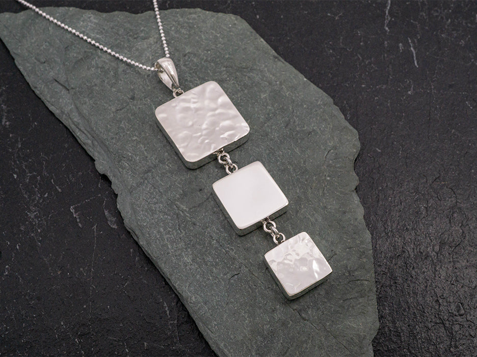 A sterling silver pendant featuring three squares of decreasing size stacked together. The top and bottom square are hammered while the middle one is smooth.