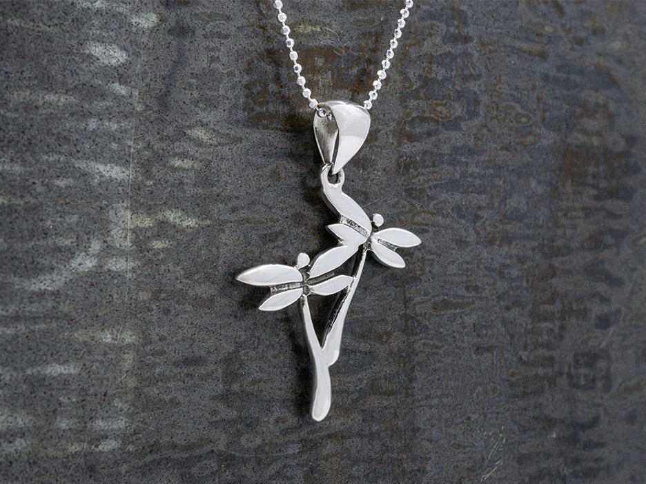 A sterling silver pendant in the shape of two dragonflies in flight hanging on a beaded silver chain.