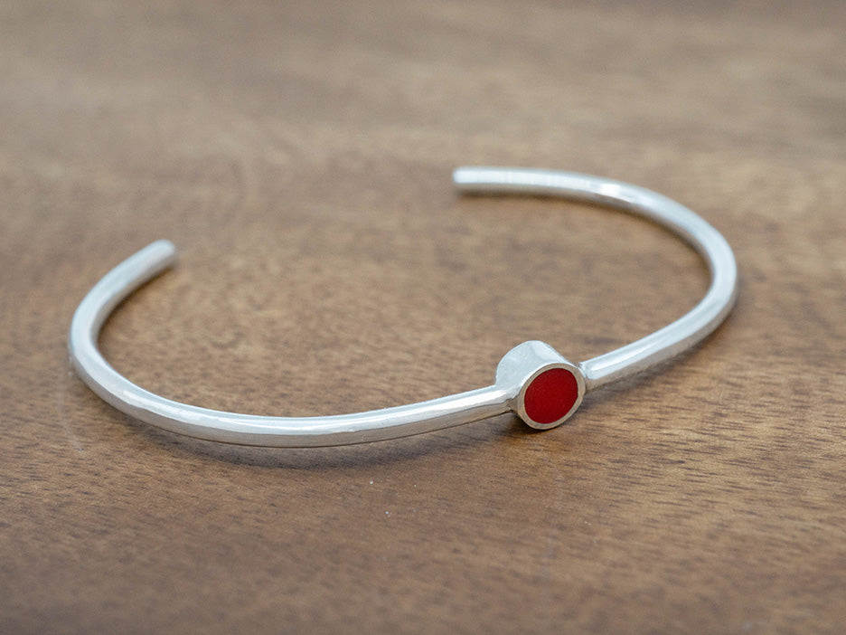 a simple silver cuff bracelet with a red enamel circle in the center