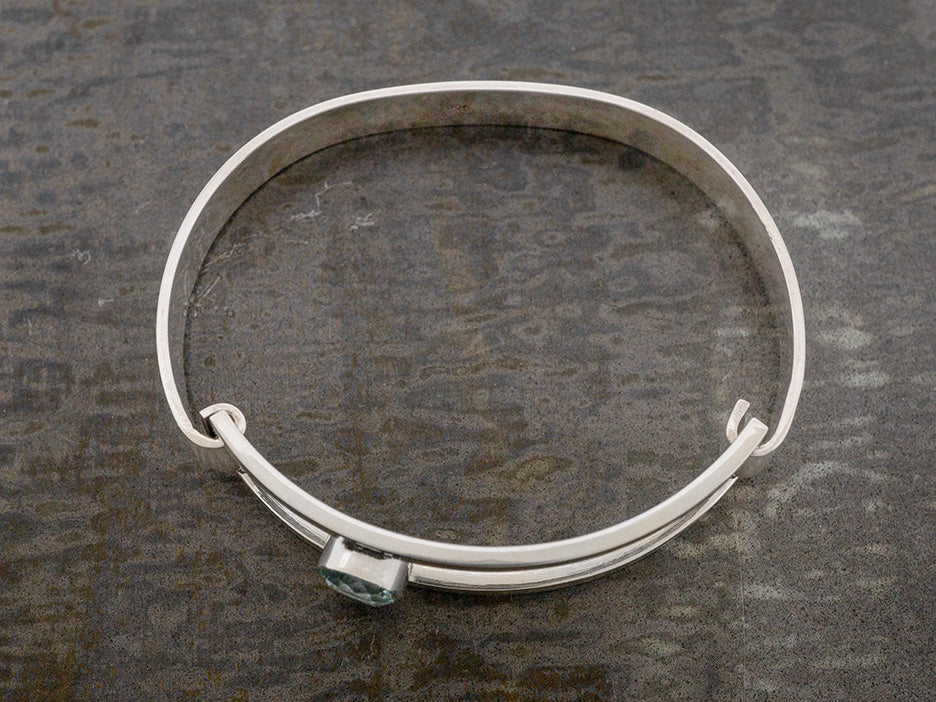 A sterling silver hinged bangle with an off-center blue crystal 