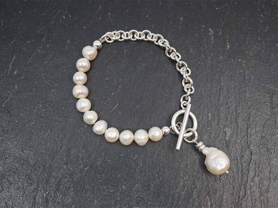 A linked bracelet that is half pearls and half silver chain. Featured a toggle finish with a dangling baroque pearl.
