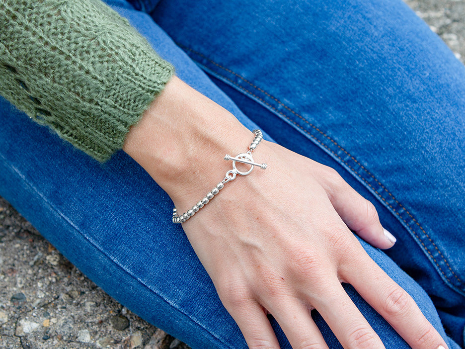 A model wearing a sterling silver beaded bracelet with a toggle closure.
