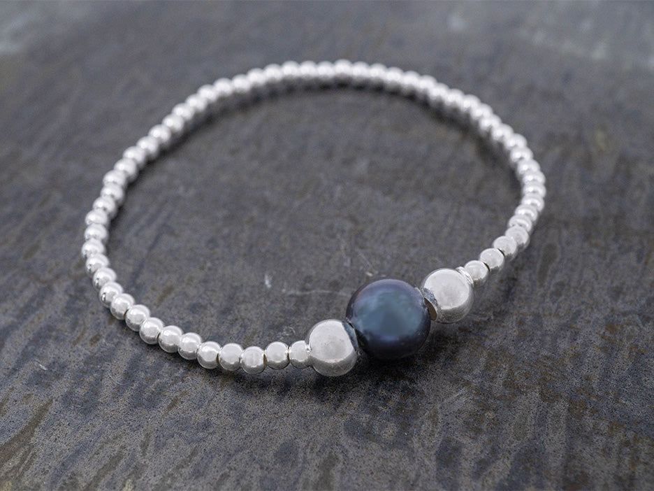 a stretchy sterling silver bead bracelet with a large black pearl in the center, flanked by two larger silver beads.