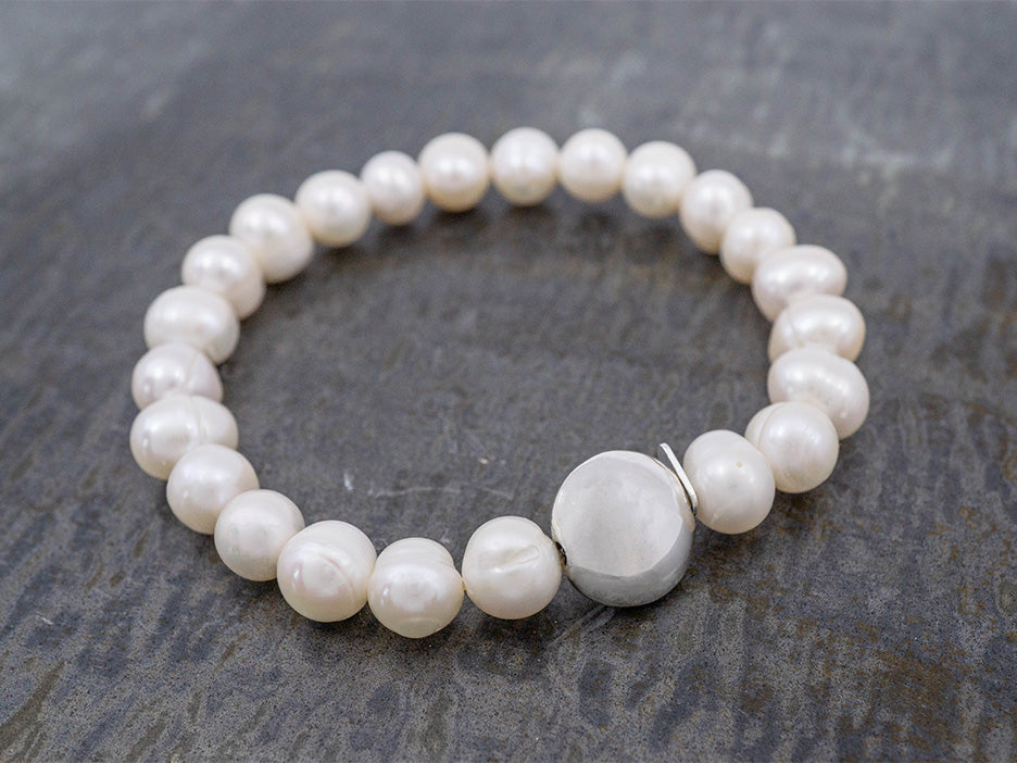 a stretch pearl bracelet with a puffed silver disc in the center
