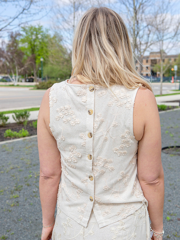 Woman wearing an off-white top with gold buttons on the back outdoors.
