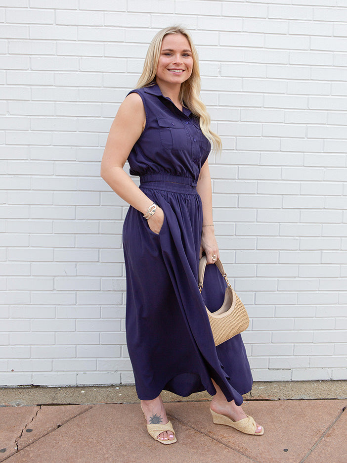 Woman in a purple tank and matching skirt standing against a white brick wall