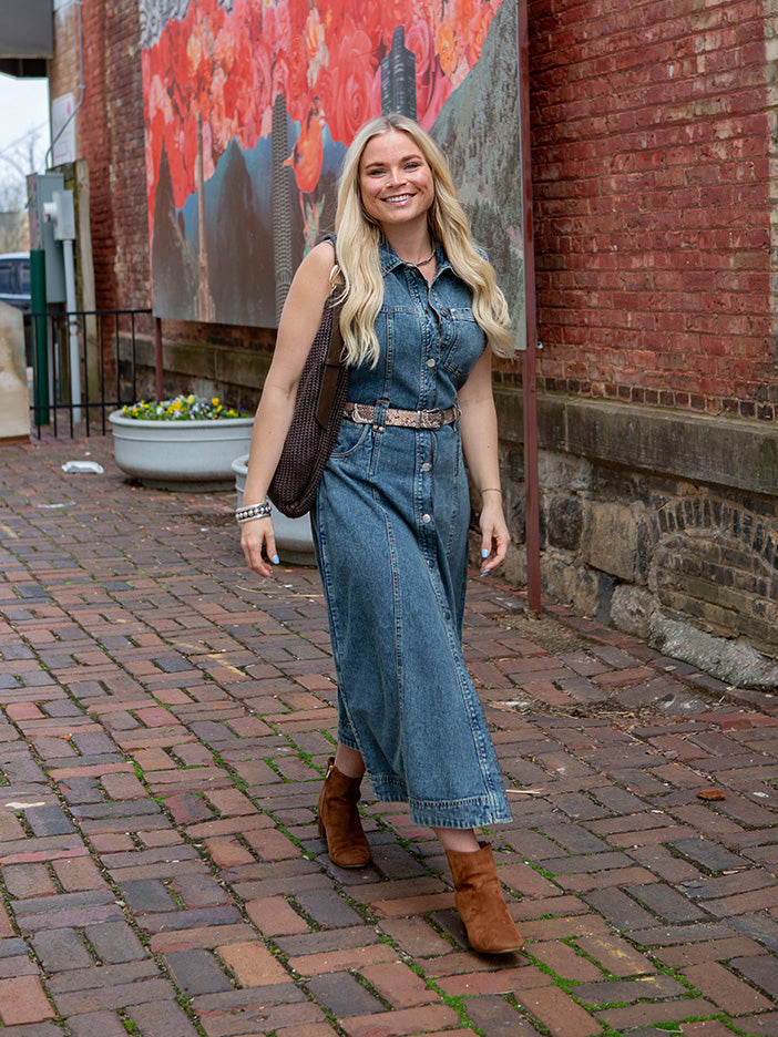 woman walking on cobblestones wearing a denim dress with a large brown handbag