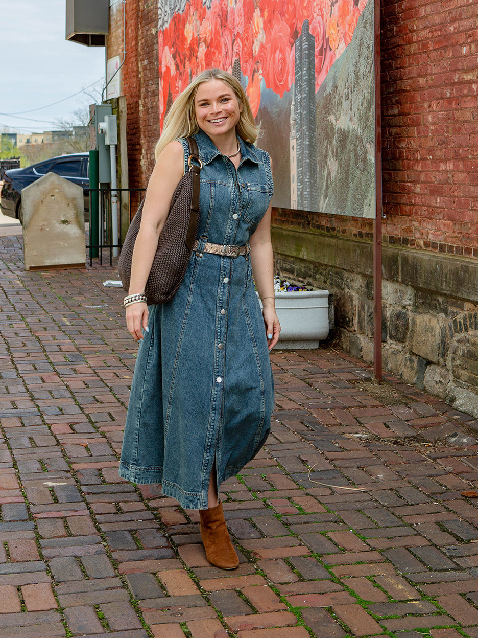 woman walking on cobblestones wearing a denim dress with a large brown handbag