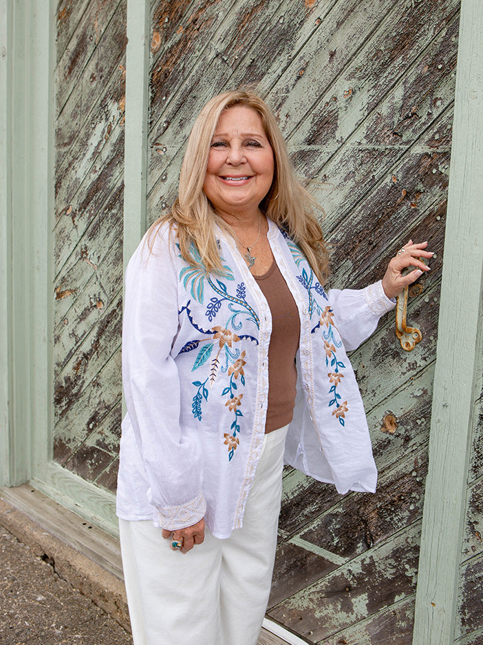 Woman wearing a white embroidered blouse standing in front of a wooden door.