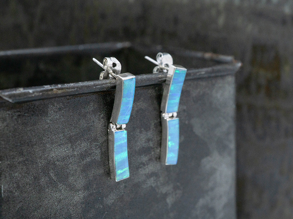 A pair of sterling silver earrings on posts. Each earring has two slightly curved rectangular links set with blue opals.
