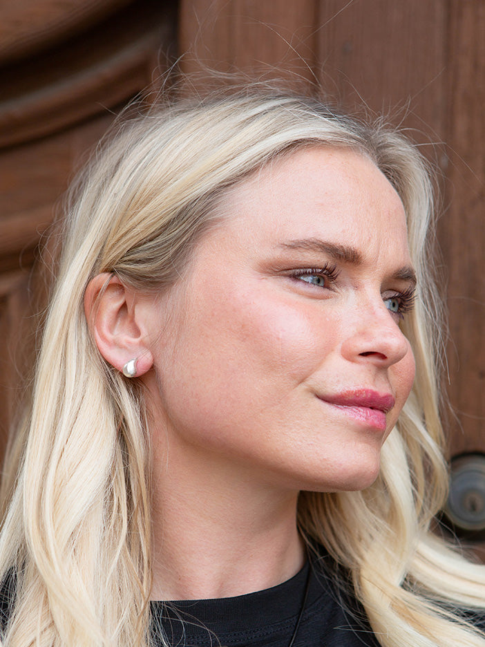 A model wearing a small, silver comma-shaped stud earring.
