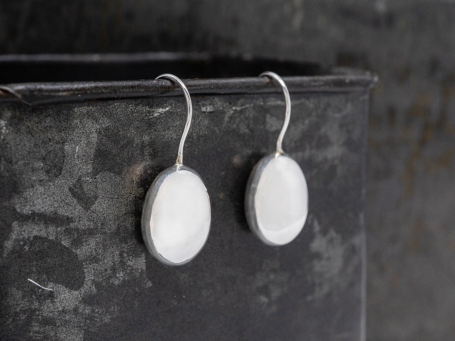 Silver earrings with white stones on a dark textured surface