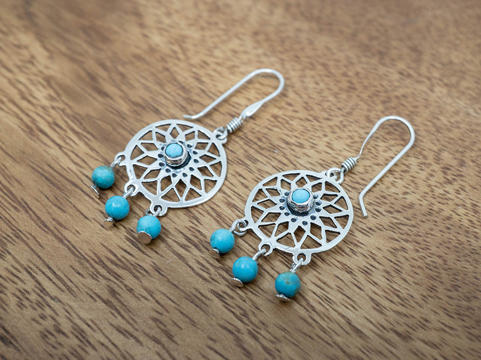 Silver dreamcatcher earrings with turquoise beads on a wooden surface