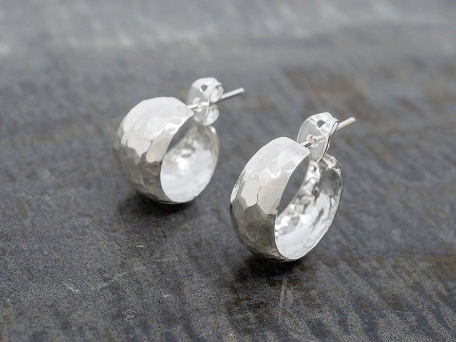 Pair of hammered silver hoop earrings on a textured gray surface