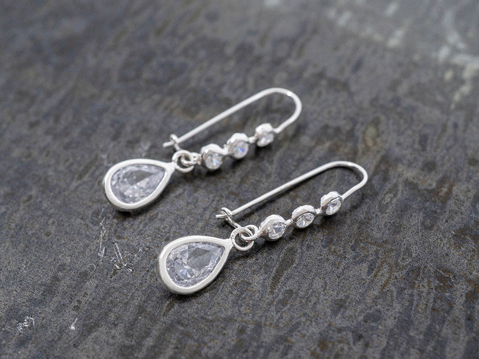 Silver teardrop earrings with clear crystals on a textured gray surface