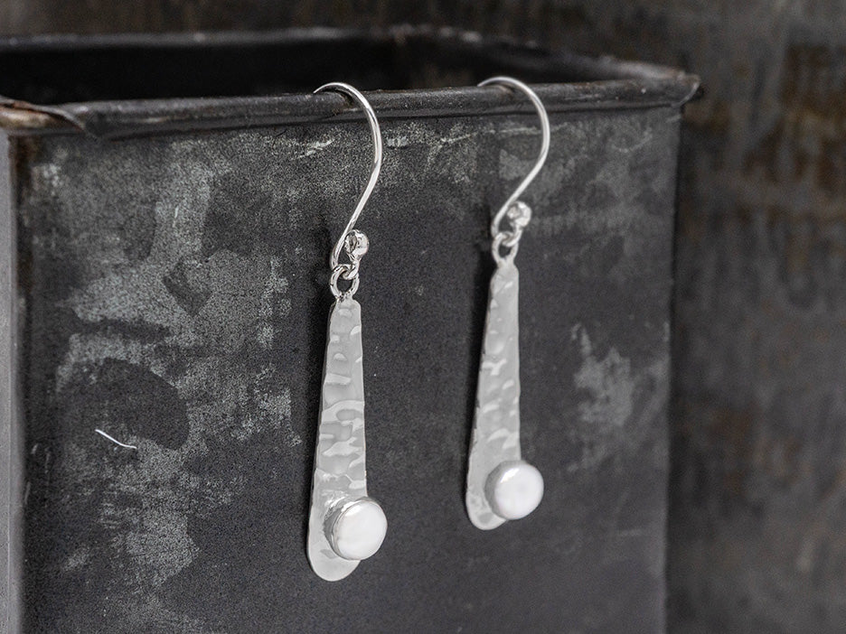 Pair of silver teardrop earrings with pearls on a black surface