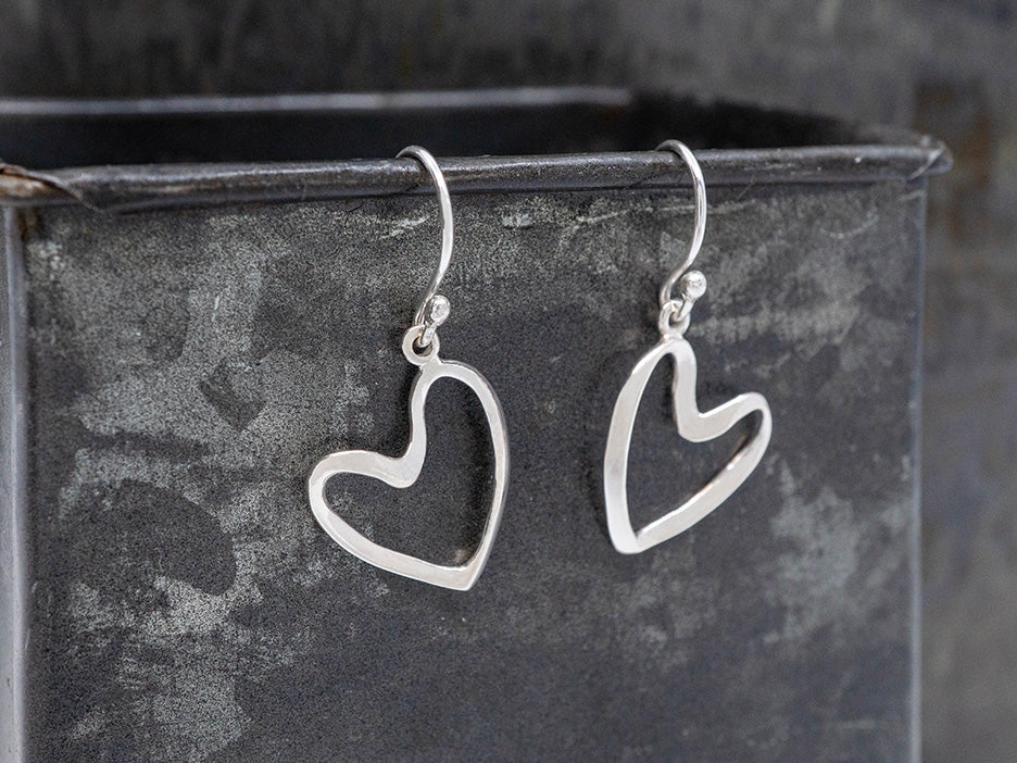 Silver heart-shaped earrings on a dark metal surface