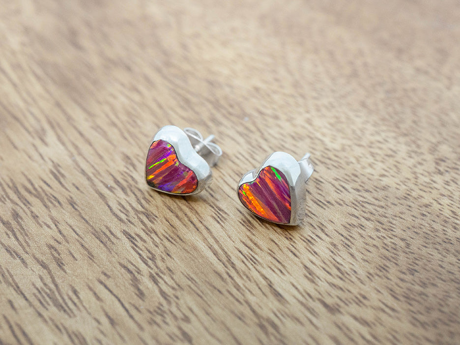 silver heart studs with pink opal inlay on a wooden surface