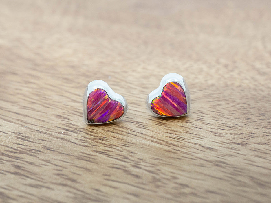 silver heart studs with pink opal inlay on a wooden surface