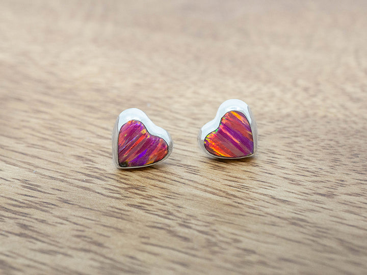 silver heart studs with pink opal inlay on a wooden surface