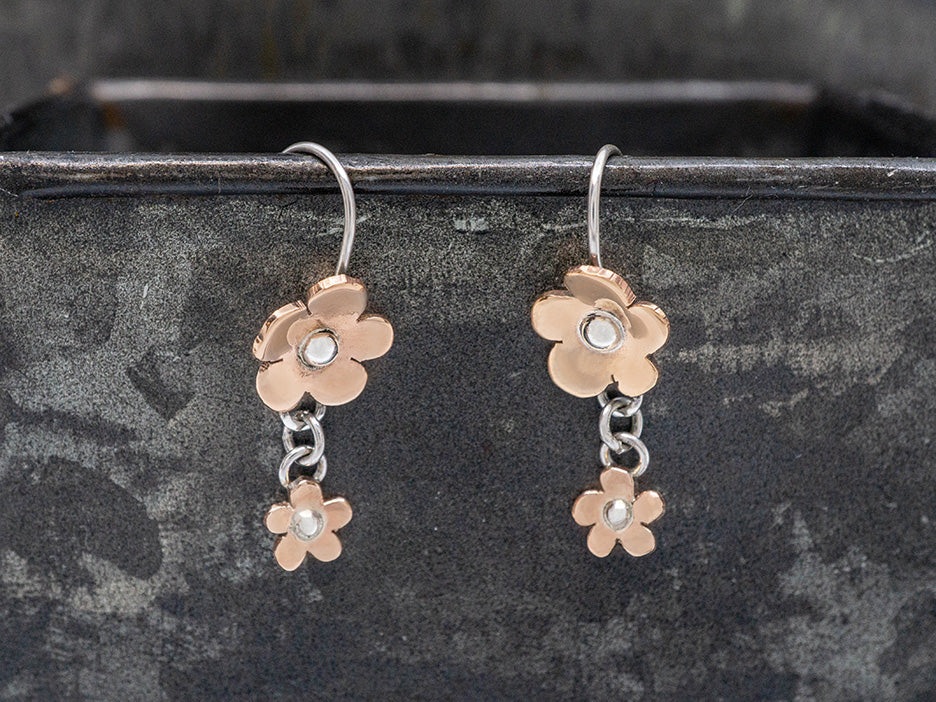 Copper flower earrings with silver centers on a dark metal background