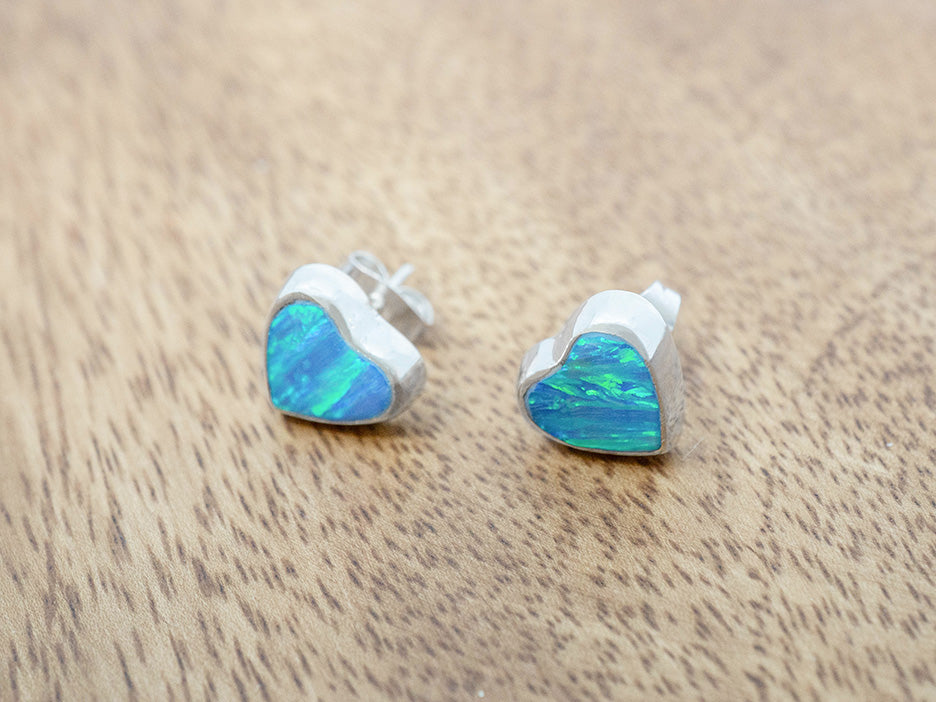 Opal heart-shaped stud earrings on a wooden surface