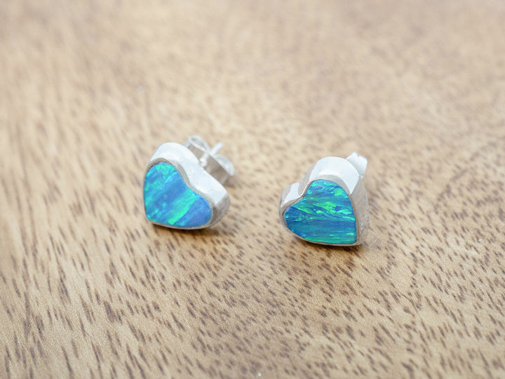 Opal heart-shaped stud earrings on a wooden surface